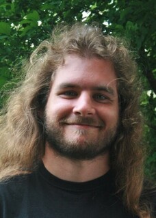 Jonas Schwab mit lockigem, langem Haar und Bart, vor grünem Hintergrund.